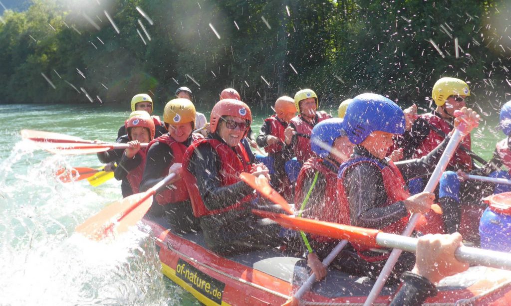 Eine Rafting Tour in der Gruppe auf der Isar. Das Wasser spritzt.