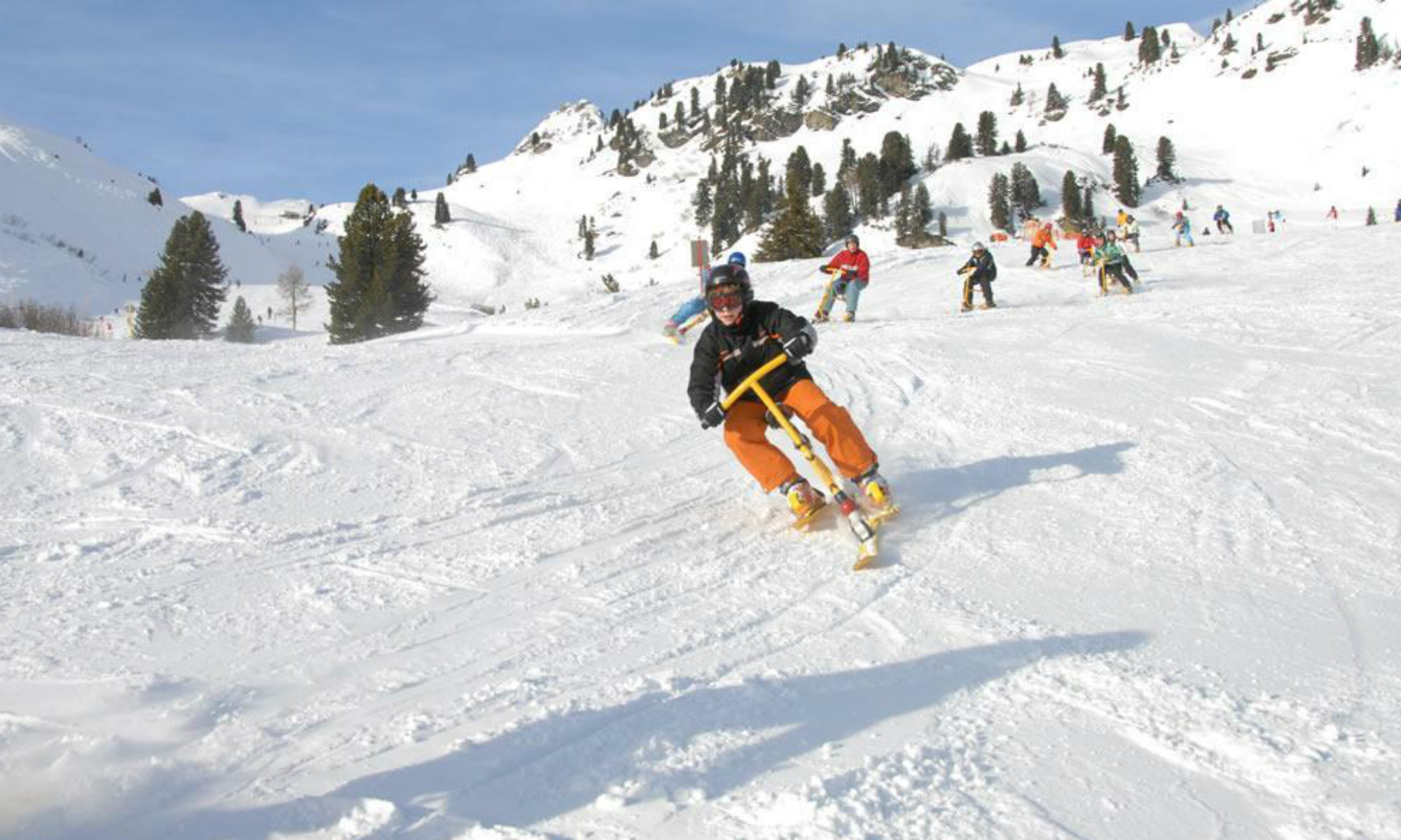 Mehrere Personen machen mit Snowbikes Kurven auf der Piste.
