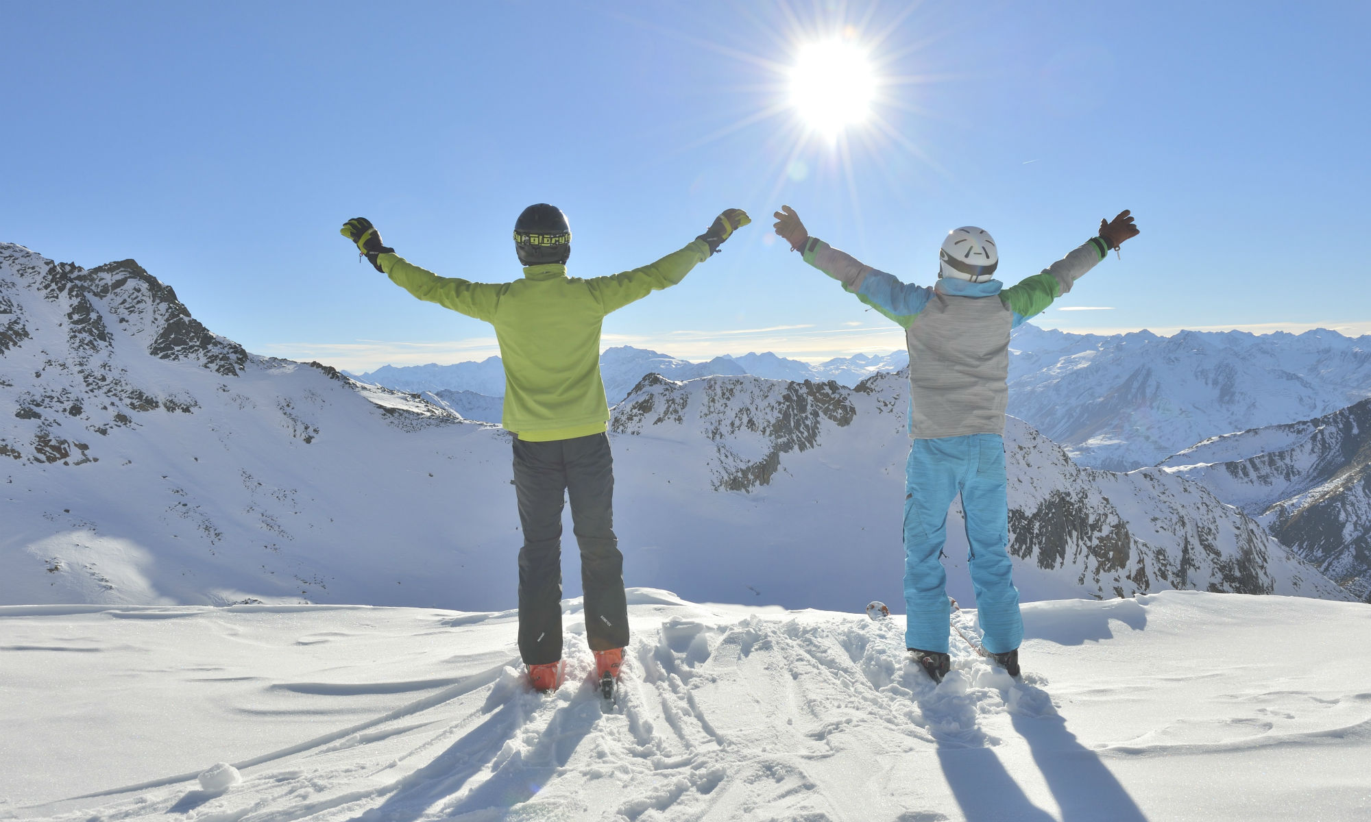 Deux skieurs profitent du soleil en haut d’une montagne.