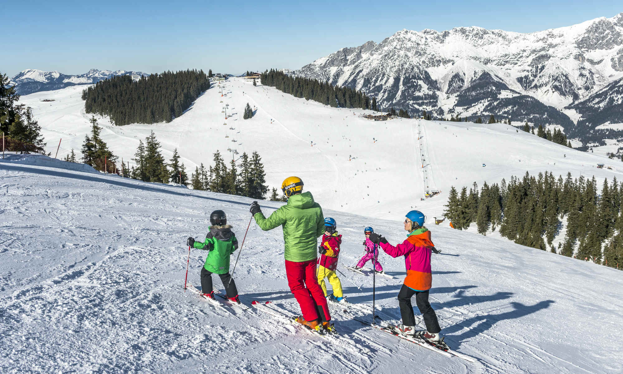 Eine Familie beim Skifahren auf der Piste mit Bergpanorama.