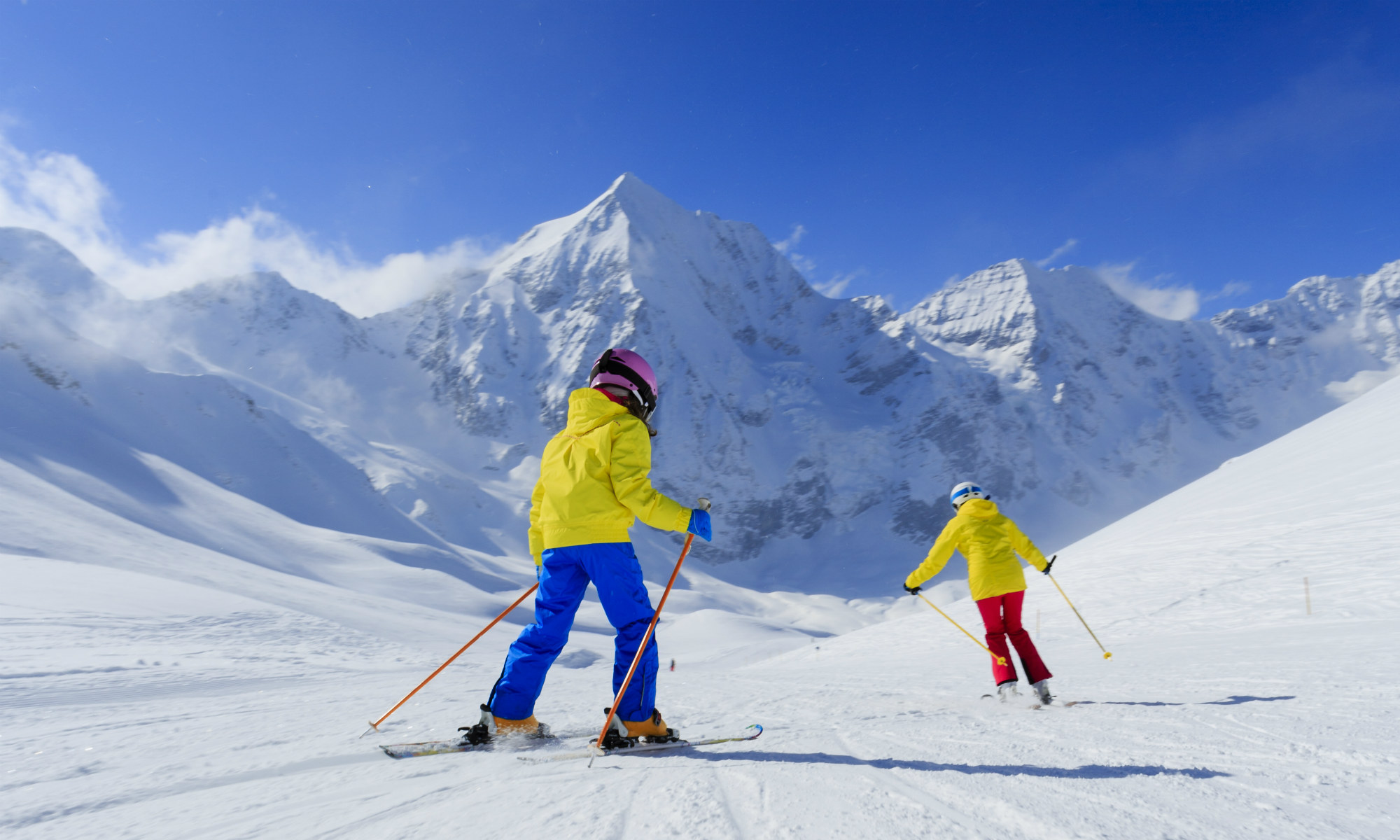 Zwei Skifahrer auf einer Piste in den Bergen.