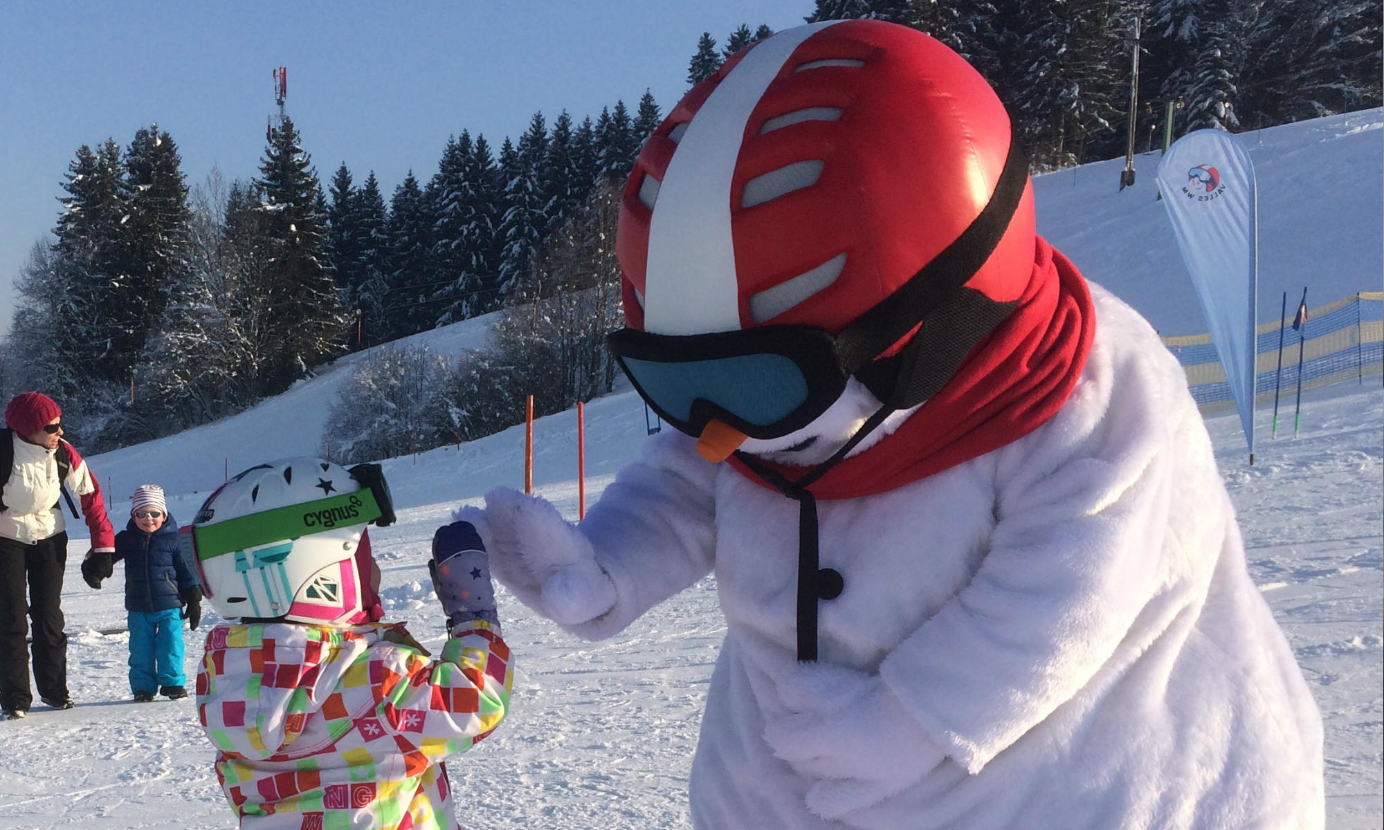 Das Maskottchen Valle klatscht mit einem Mädchen auf der Skipiste ein.