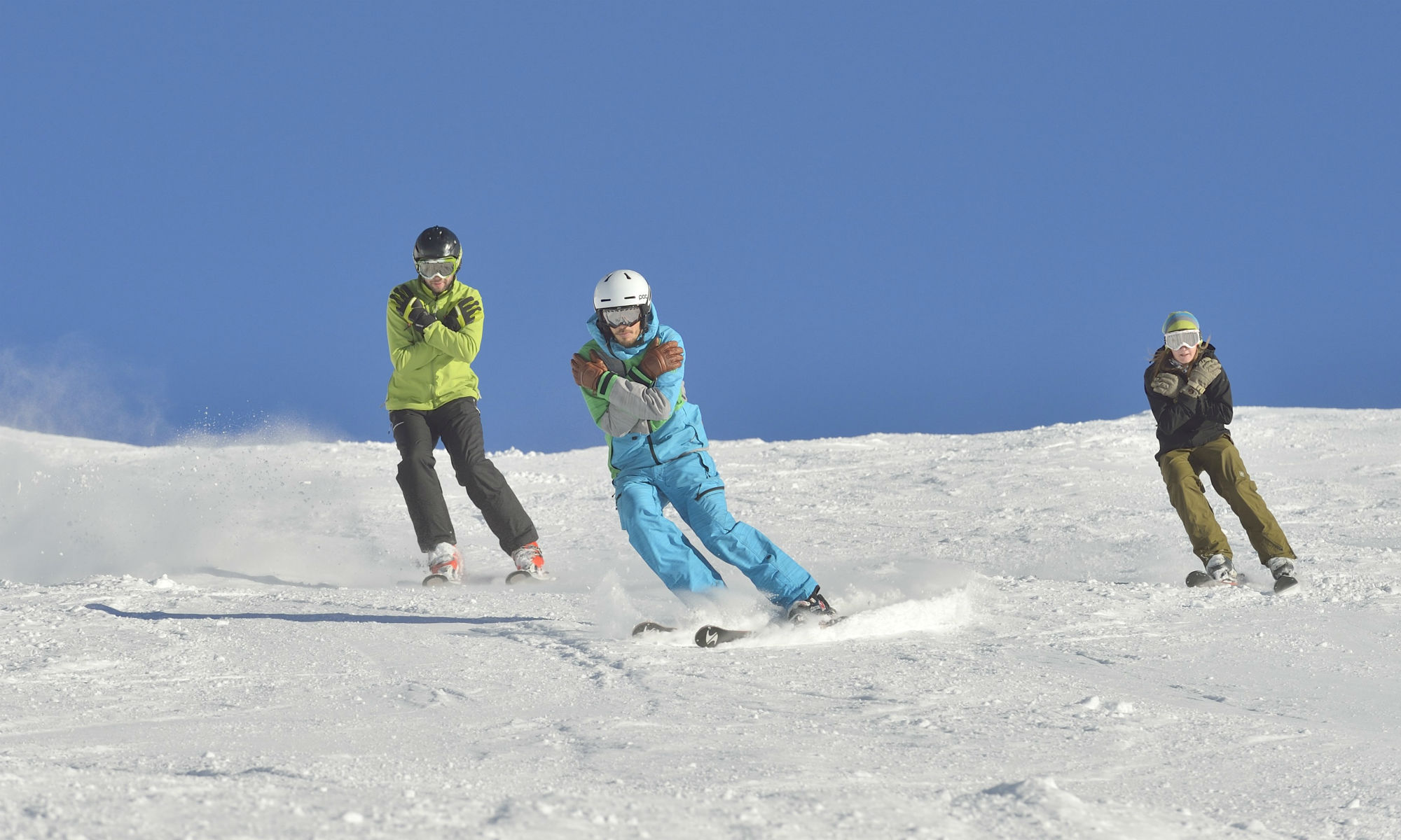 Privater Skilehrer mit 2 fortgeschrittenen Skifahrern beim Üben auf der sonnigen Piste.