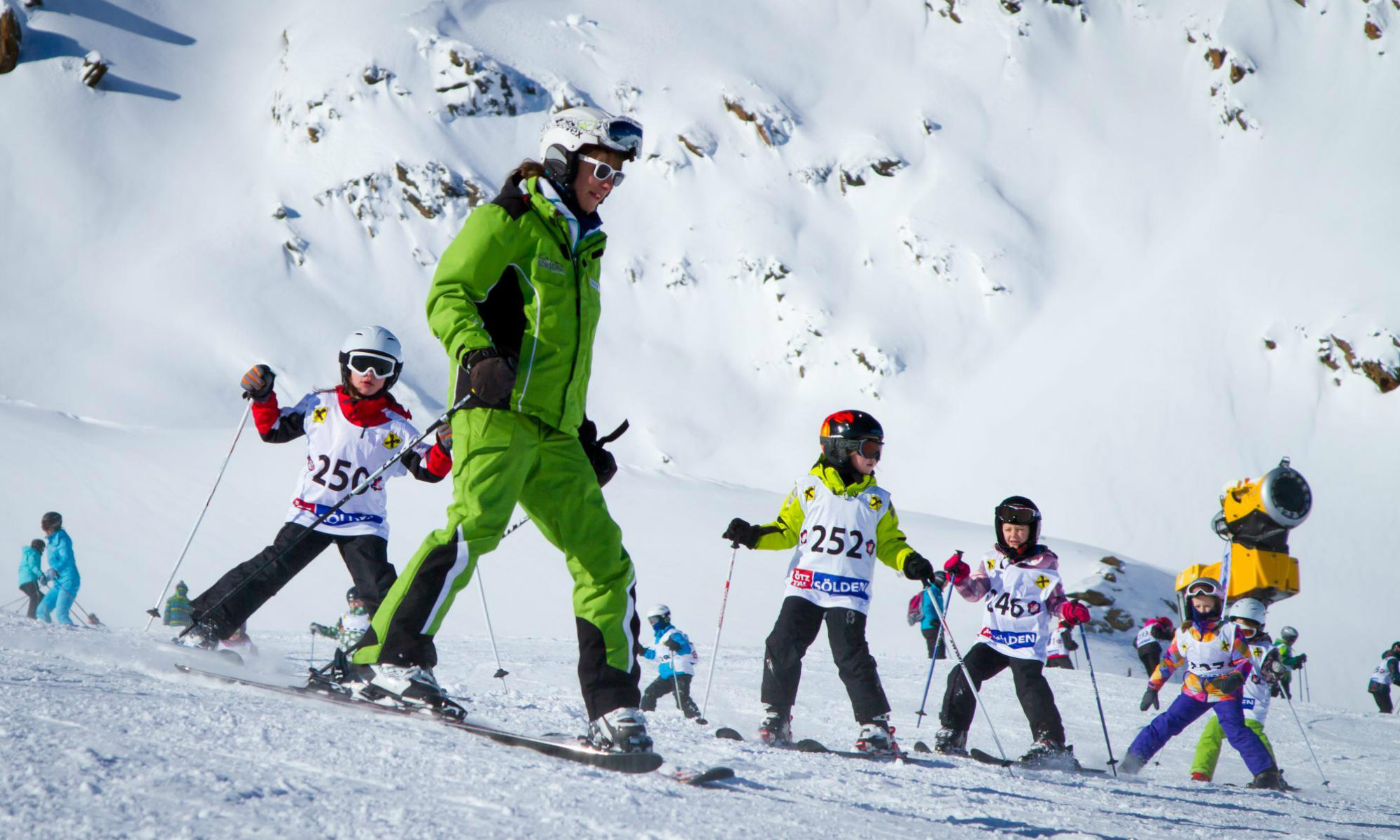 Ein Skilehrer bringt 5 Kindern das Skifahren auf einer Piste im Skigebiet Sölden bei.