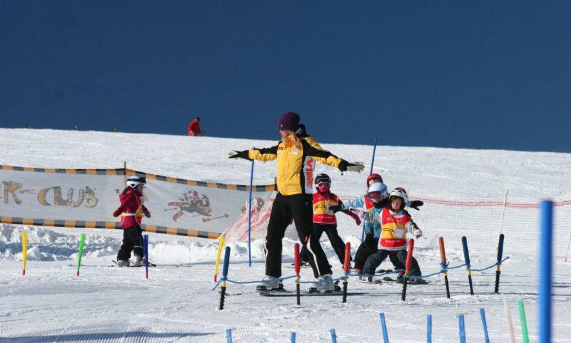 Eine Skilehrerin fährt mit einer Gruppe Kinder im Pflug durch das Kinderland.