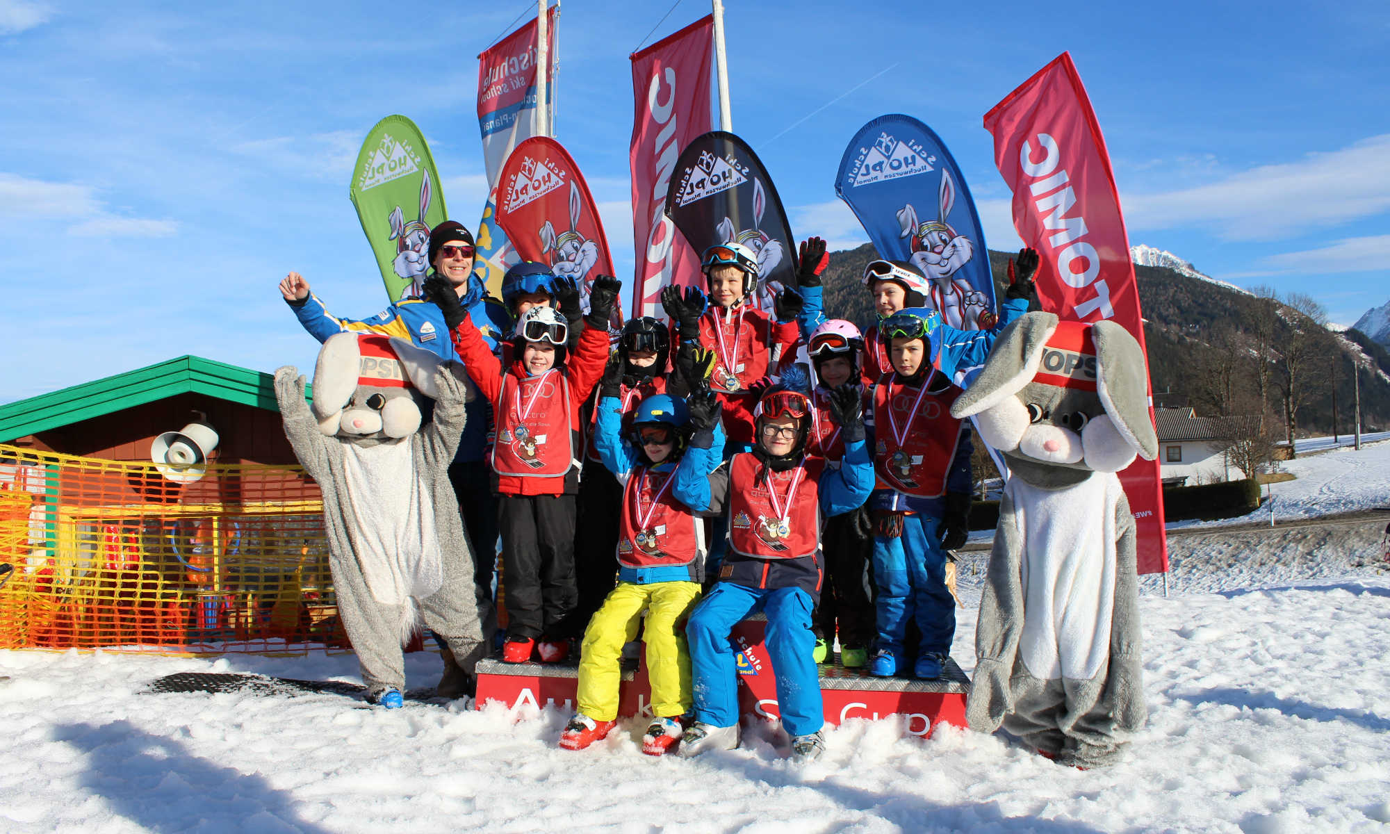 Eine Gruppe Kinder und das Maskottchen Hopsi freuen sich bei der Siegerehrung nach dem Skikurs in Schladming.