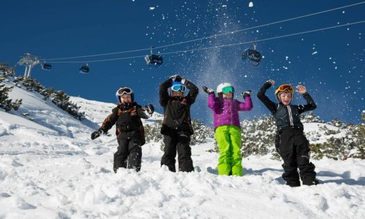 4 children playing in the powdery snow of Lermoos with the cable car in the background.