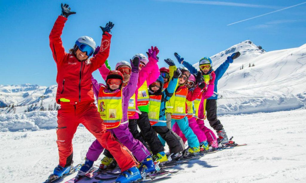 A group of happy kids during a ski lesson with their instructor skiing on a sunny slope in Flachau.