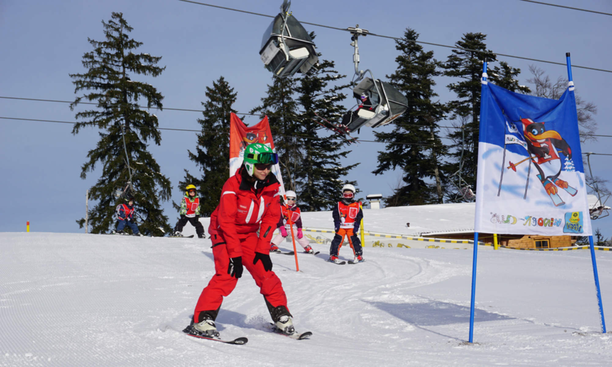 Eine Skilehrerin bringt Kindern im Kinderland das Kurvenfahren im Pflug bei.