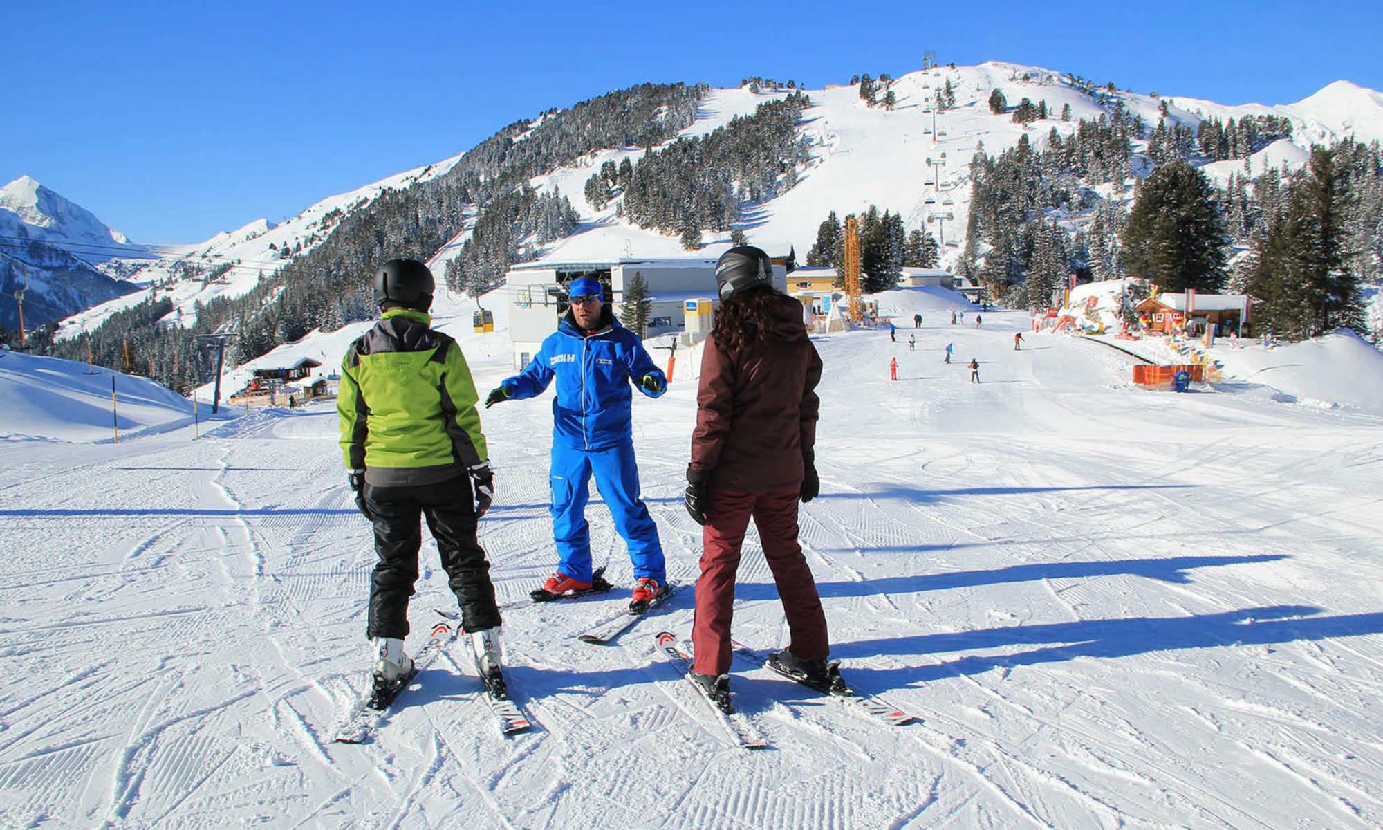 Ein privater Skilehrer zeigt zwei Erwachsenen die richtige Skitechnik im Skigebiet Mayrhofen.