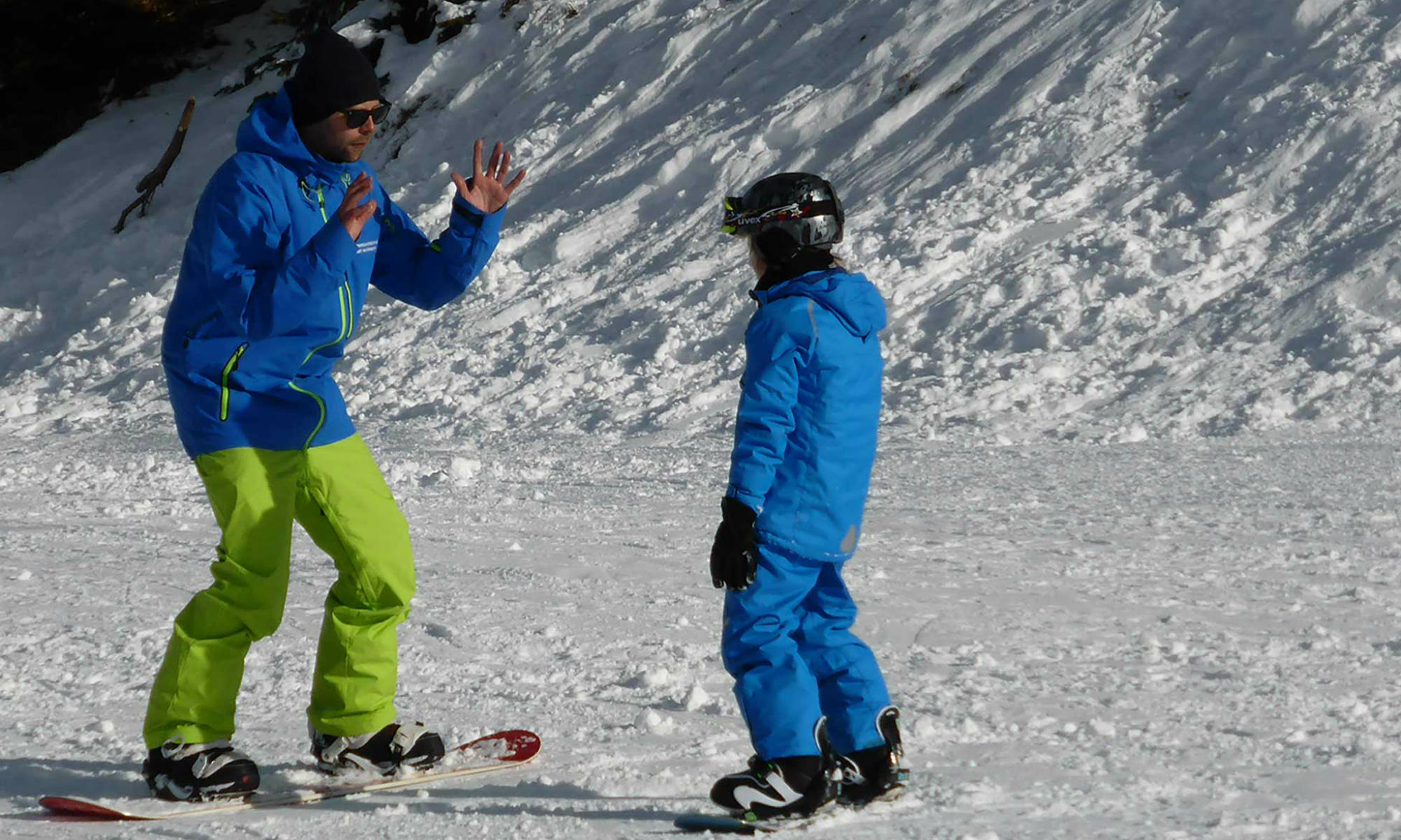 Ein Privatlehrer zeigt einem Kind die richtige Technik im Snowboarden auf einer flachen Piste im Skigebiet Mayrhofen.