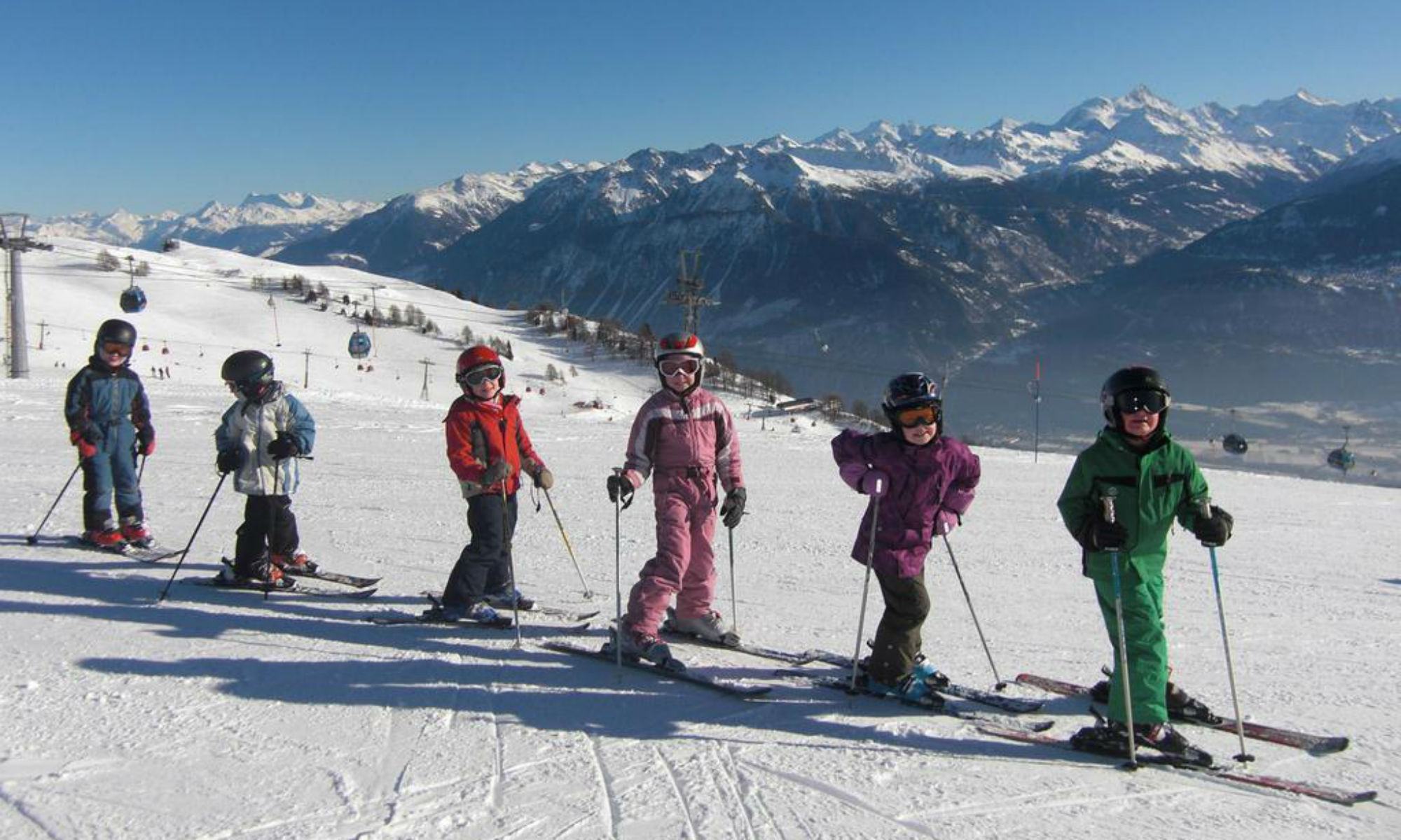 Eine Gruppe von Kinder beim beim Skifahren lernen im Wallis auf einer sonnigen Piste in Crans-Montana.