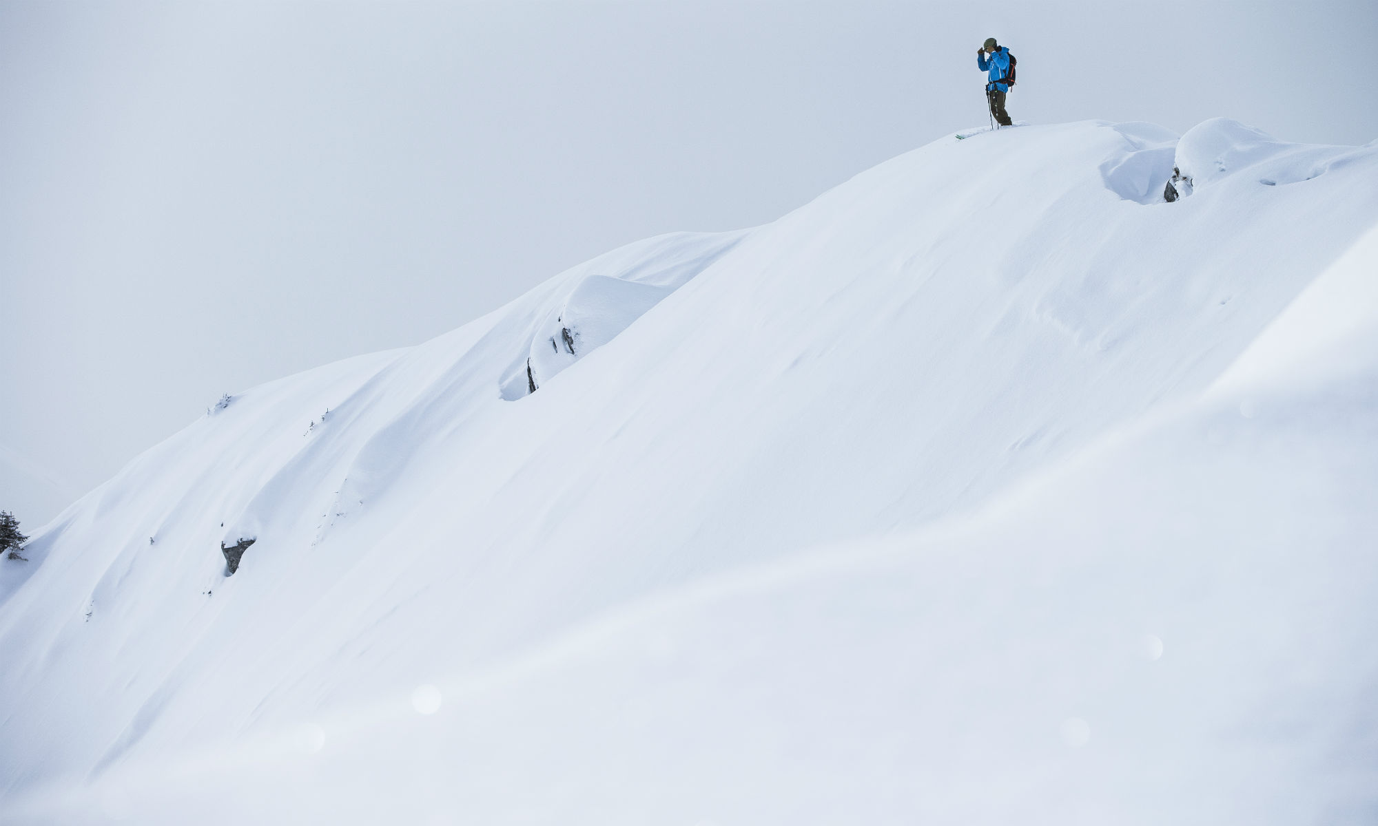 Skifahrer blickt von einer Wechte aus in einen tief verschneiten Hang in Laax.