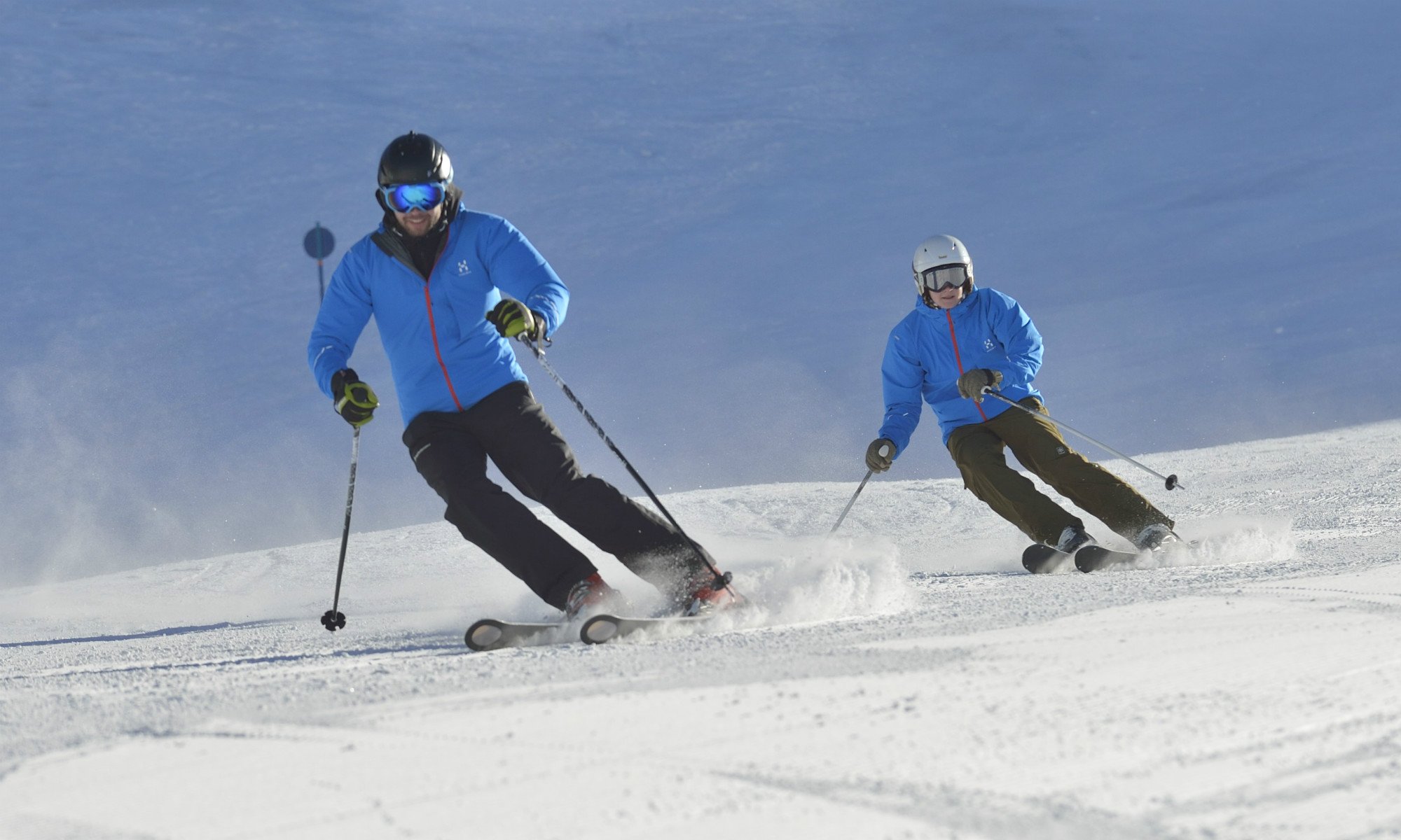 Two skiers skiing down the piste doing parallel turns.