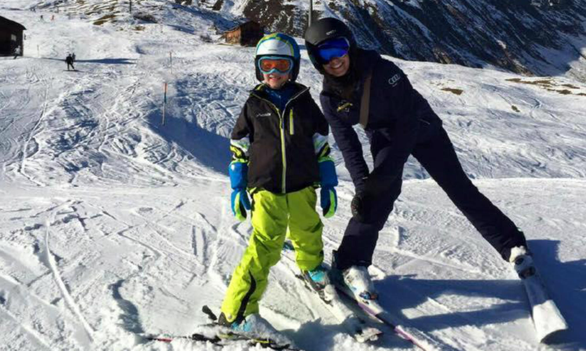 Eine Skilehrerin und ein Junge stehen im Pflug auf einer Piste im Skigebiet Andermatt.