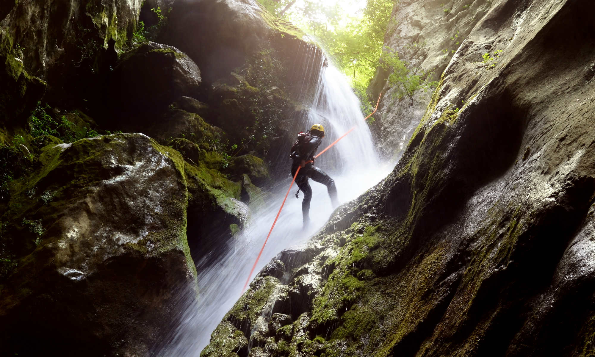 Ein Mann seilt sich beim Canyoning an einem Wasserfall in einer Schlucht ab.