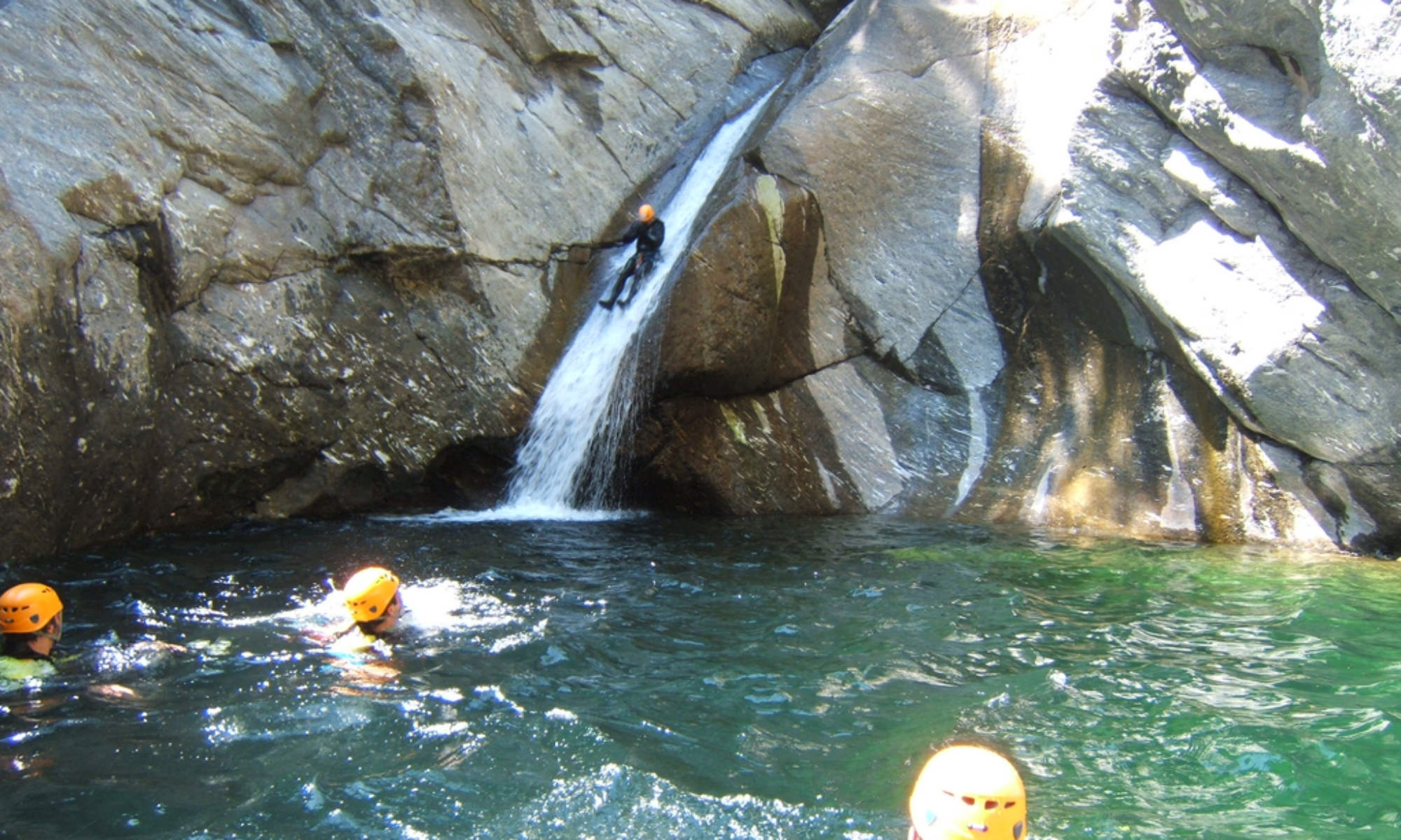 Teilnehmer ein Canyoning Tour auf einer natürlichen Wasserrutsche und in einem Wasserbecken in der Schlucht Chalamy in Italien.