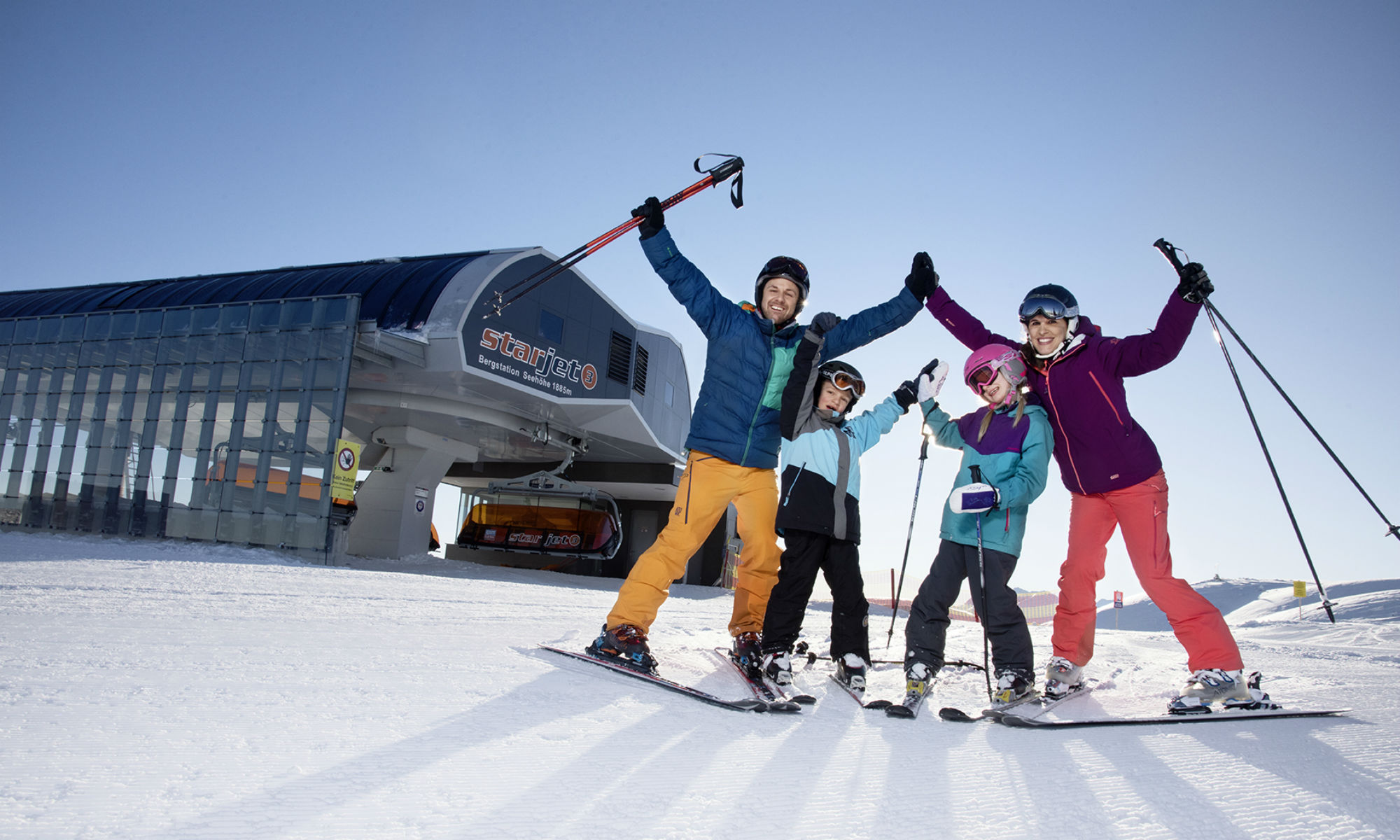 Eine Familie wirft vor der Bergstation in Flachau die Hände voller Freude in die Luft.