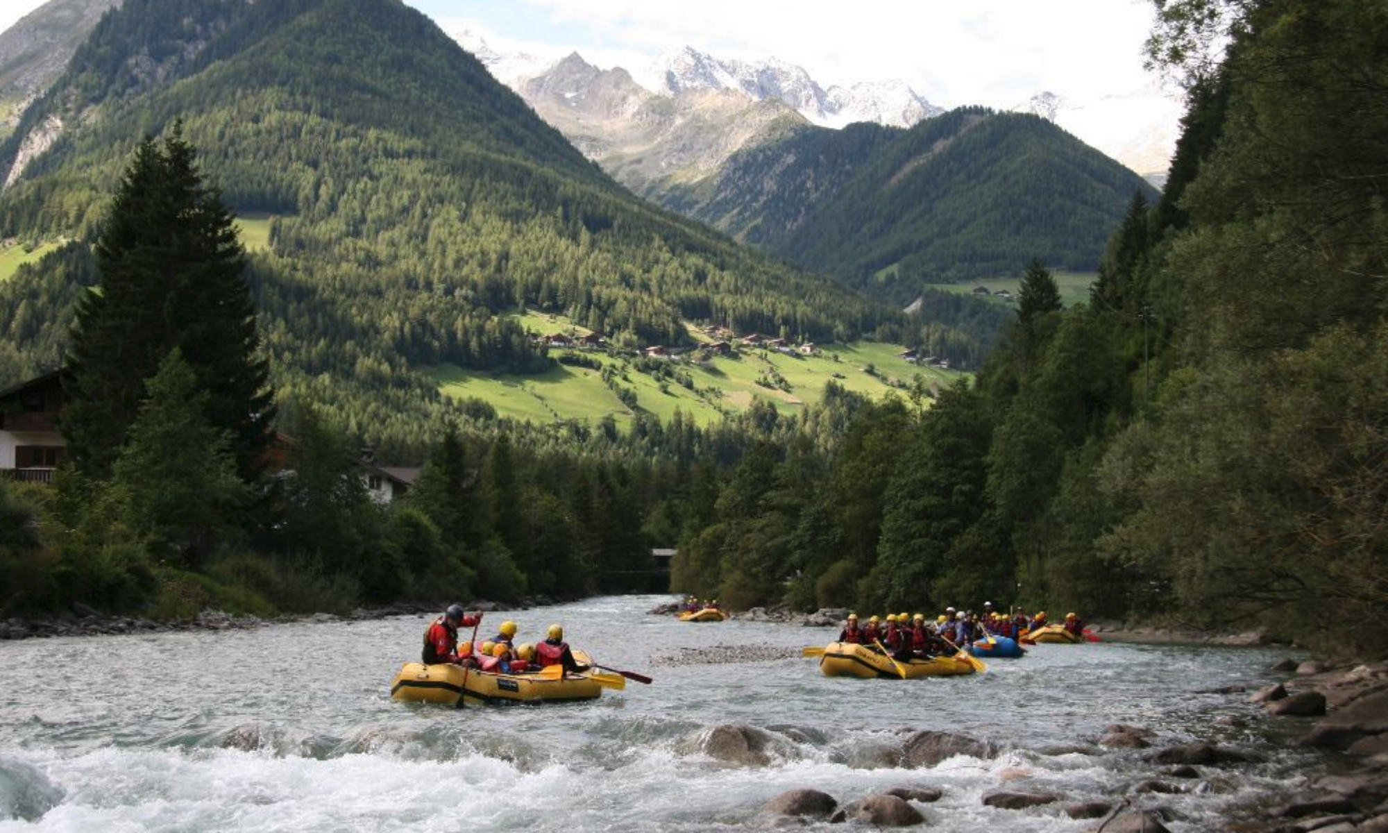 Mehrere Rafts paddeln auf einem Wildfluss in Südtirol vor dem Bergpanorama der Dolomiten.