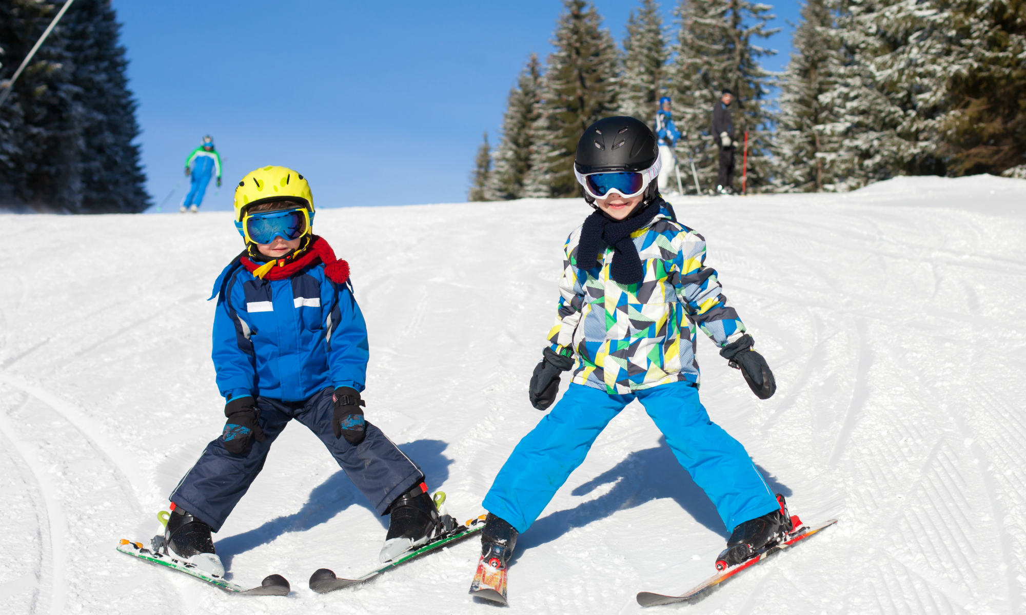 Two children skiing in plough position on a sunny ski slope.