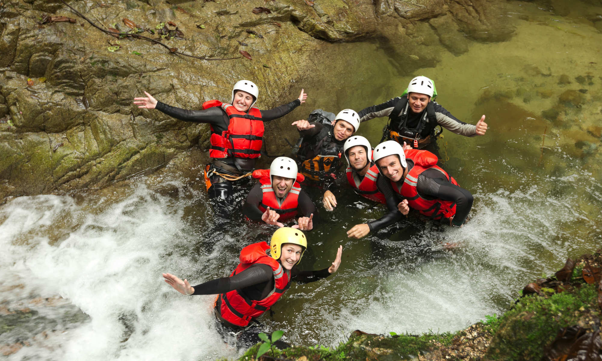 Un groupe d’amis tout sourire dans l’eau tumultueuse d’un canyon.