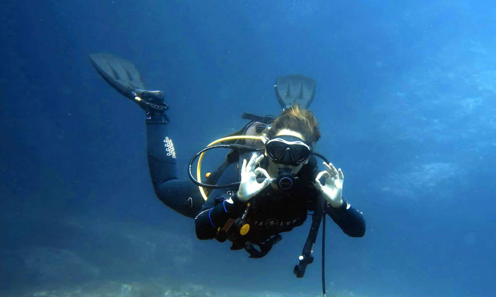 A female diver is signalling ‘O.K.’ while scuba diving in Malta.