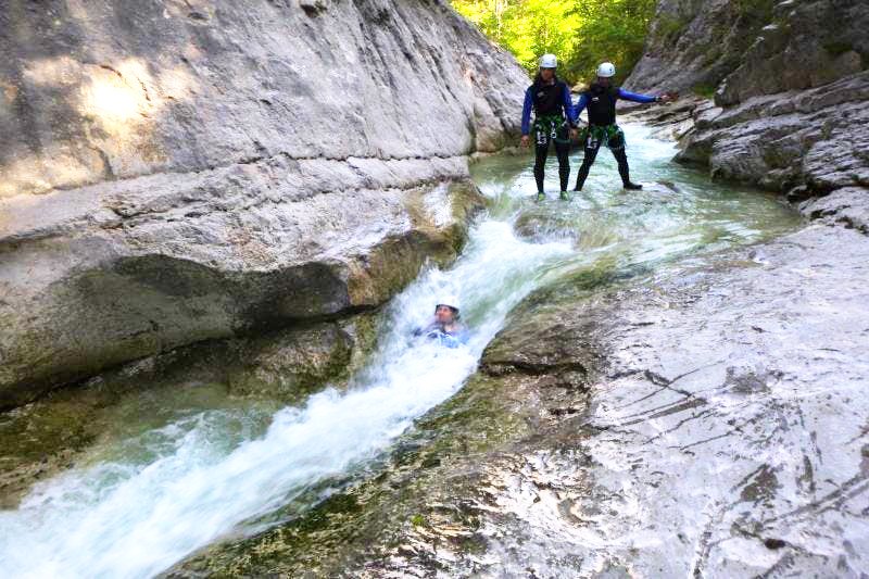  Lors de son activité canyoning dans le Verdon, une personne glisse dans un toboggan naturel dans le canyon du Haut Jabron sous les yeux de deux amis.