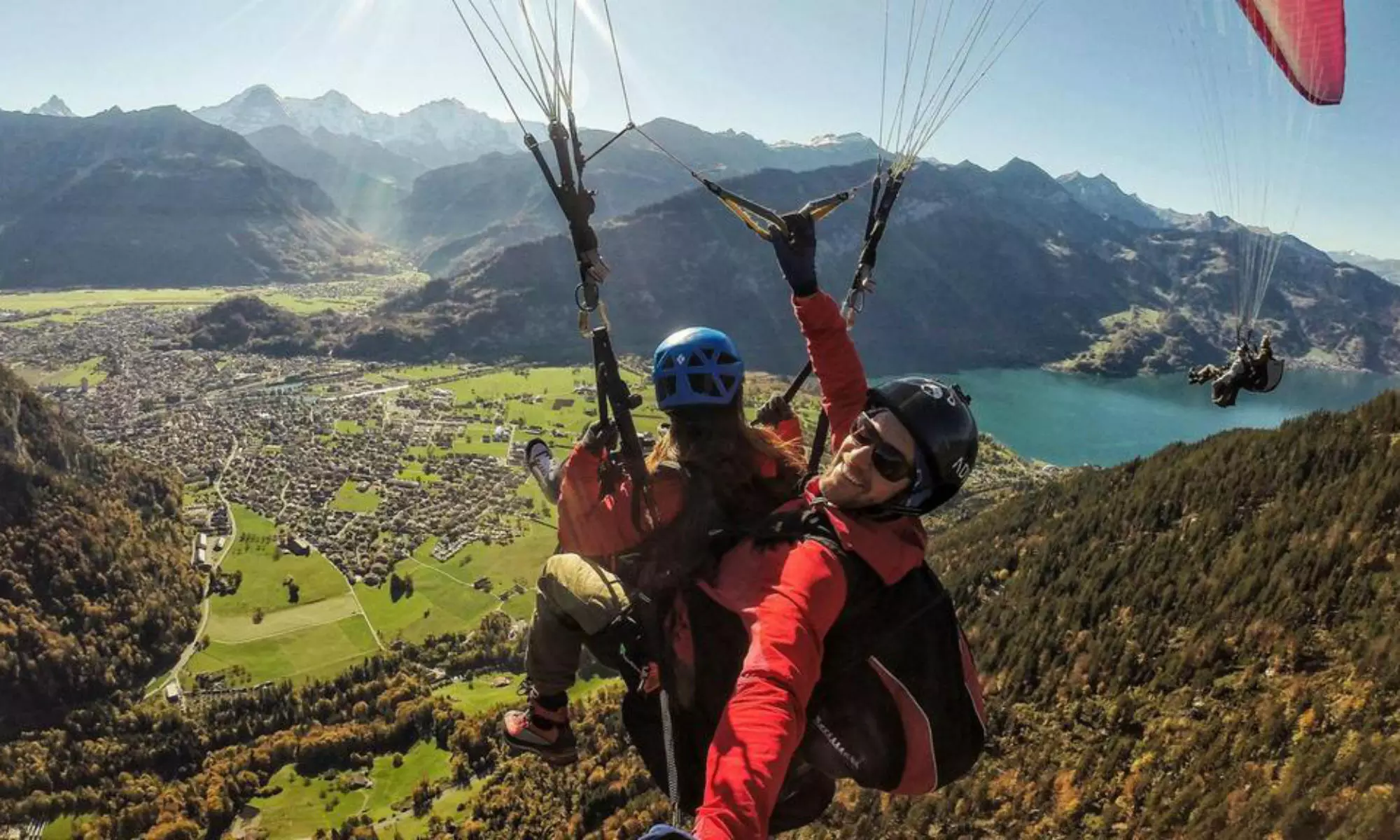 4 parapentes volent devant le panorama des montagnes et des lacs d'Interlaken.