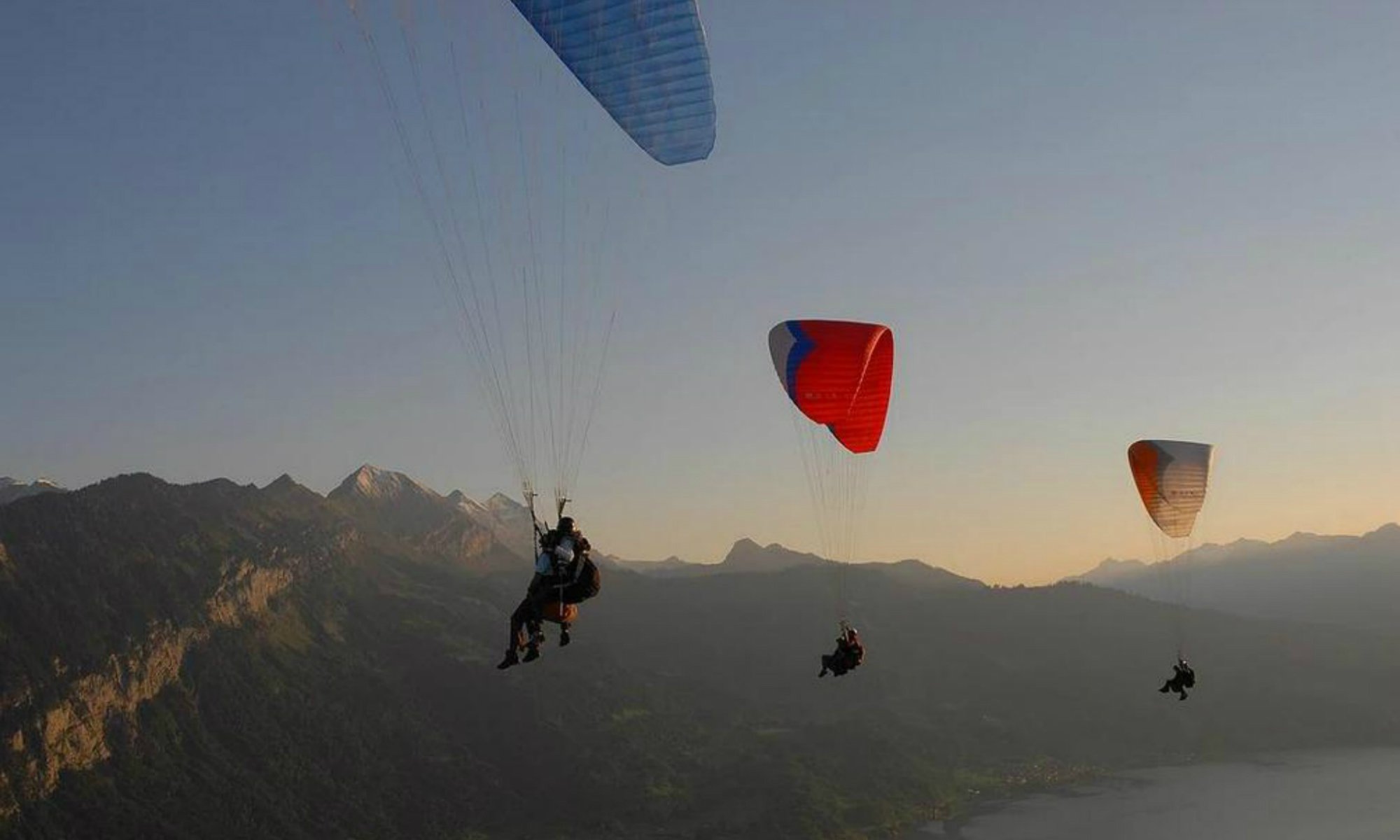 Mehrer Paraglider segeln bei Sonnenaufgang über die Berglandschaft in Interlaken.