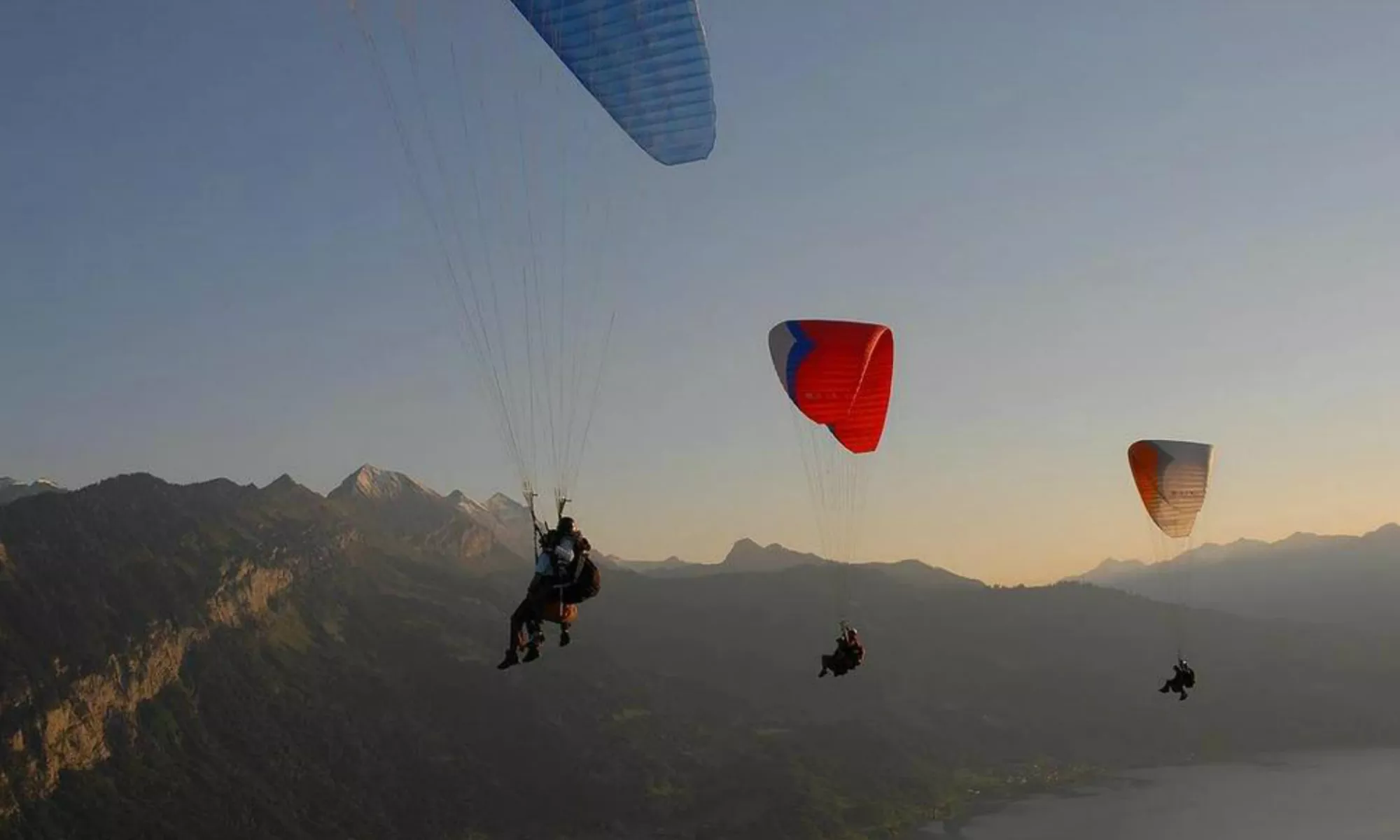 Plusieurs parapentistes survolent le paysage montagneux d'Interlaken au lever du soleil.