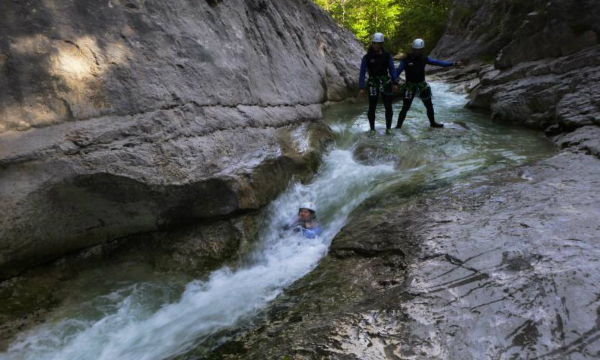 Une personne glisse dans un toboggan naturel dans le canyon du Haut Jabron sous les yeux de deux amis.