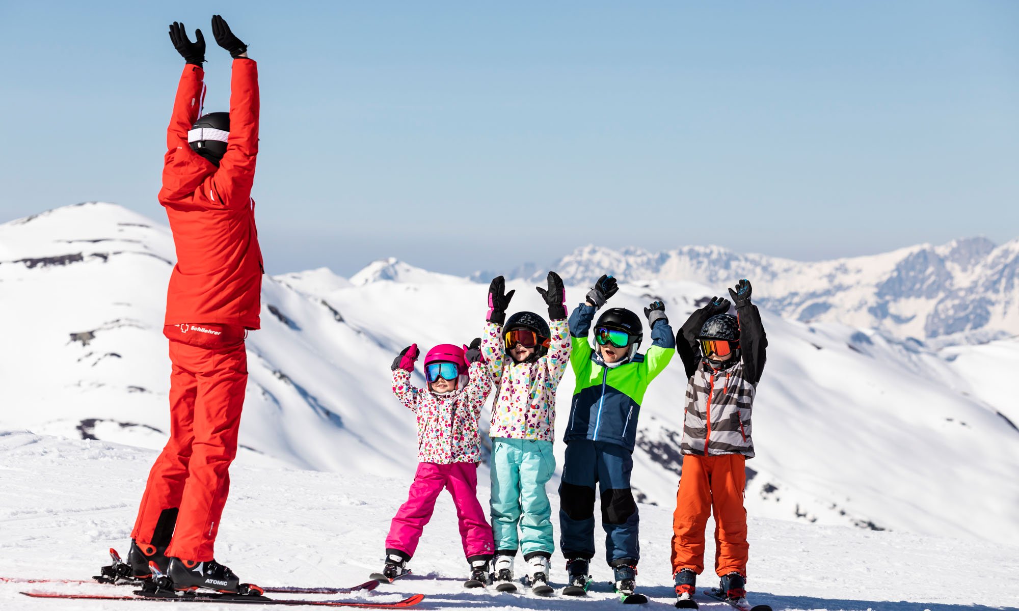 Een skileraar doet de wave met een groepje kinderen.