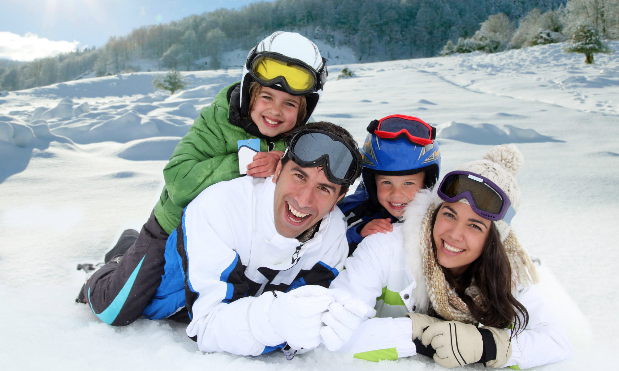 Une famille souriante pose allongée dans la neige.