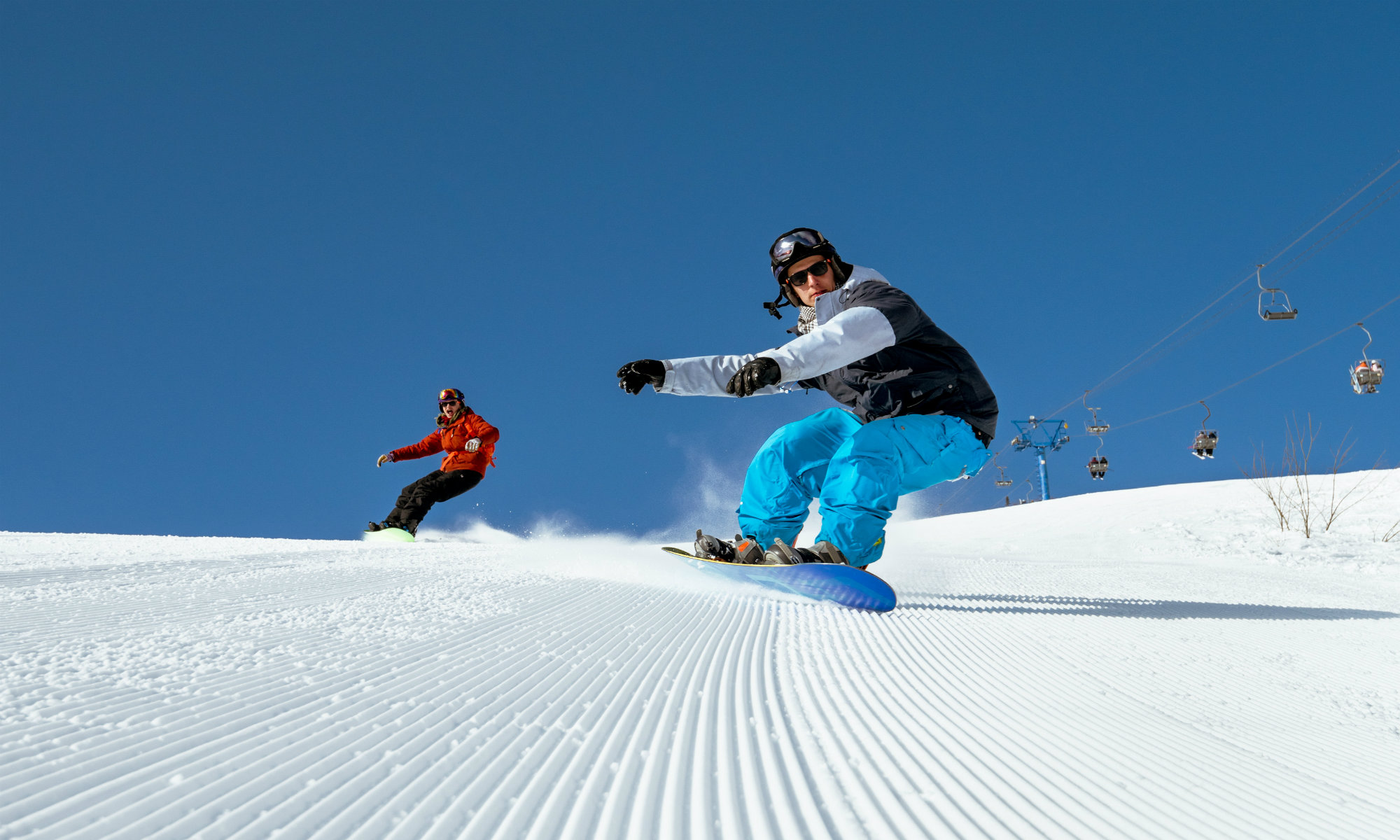 Two snowboarders boarding on freshly-groomed slopes