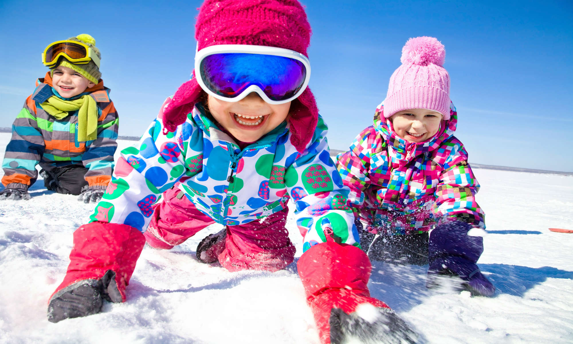 Tre bambini giocano con la neve a Bormio, mentre sorridono verso la macchina fotografica.