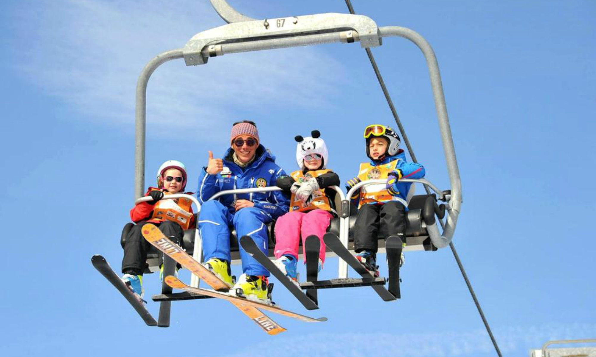 Un istruttore di sci e 3 piccoli allievi sorridono verso la macchina fotografica mentre sono sullo skilift.