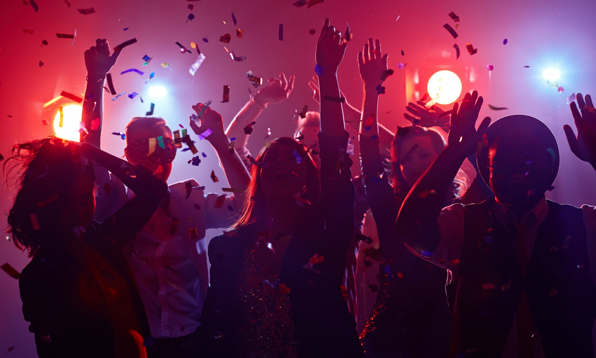 Un gruppo di amici balla in discoteca con luci soffuse e coriandoli colorati che volano per la sala.