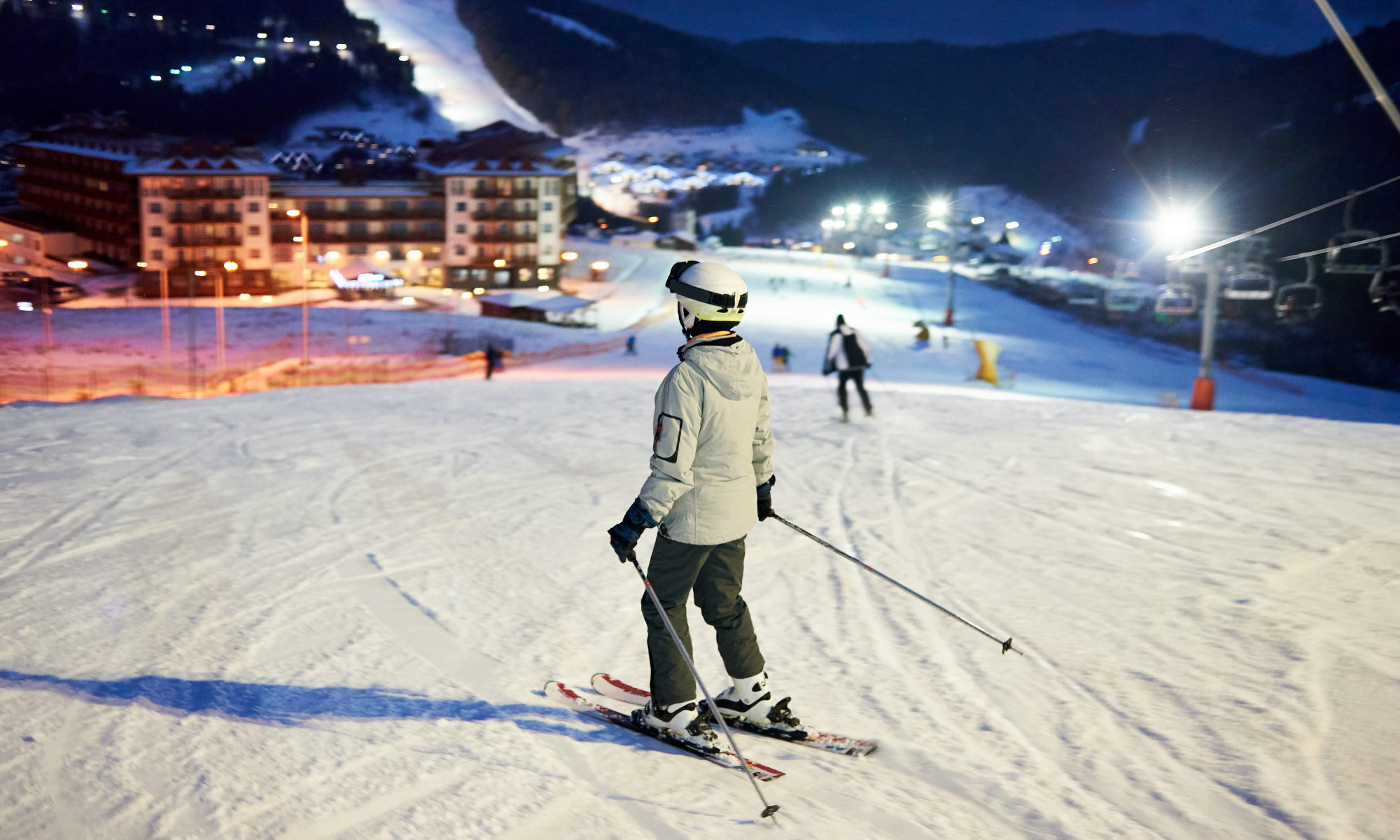 Uno sciatore in procinto di cominciare la discesa di una pista illuminata di notte.