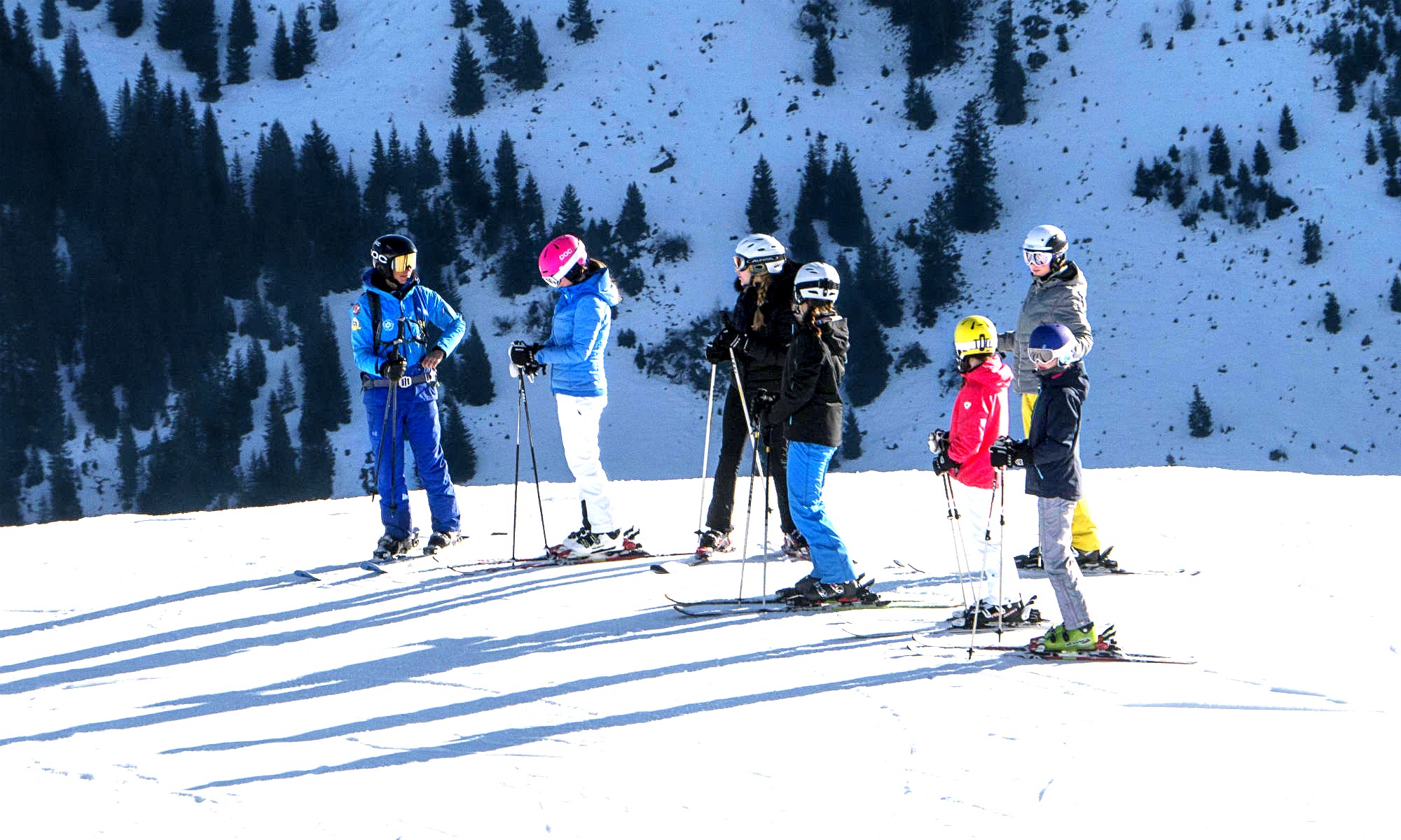 Un gruppo di 6 sciatori ascolta le istruzioni del maestro di sci.