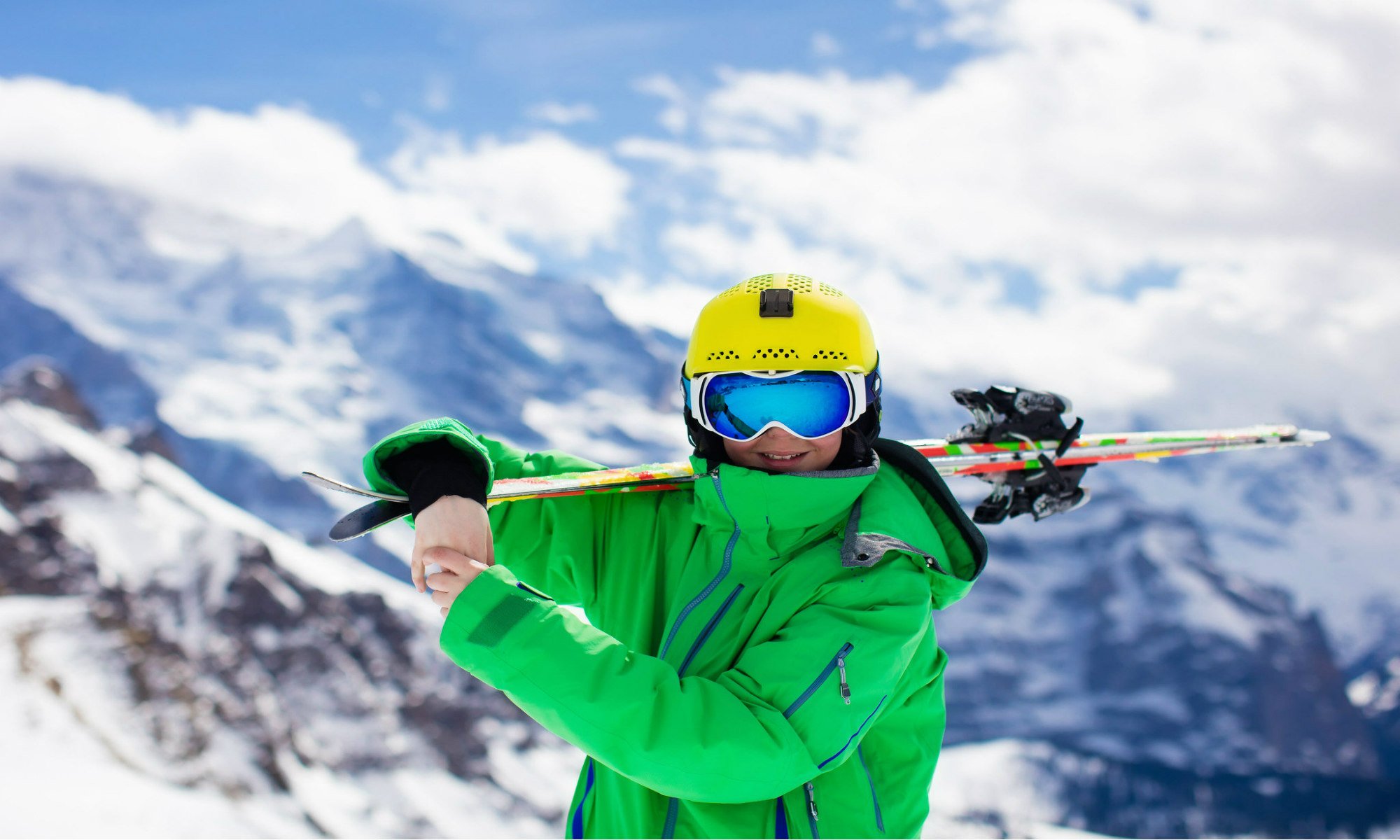 Smiling teenage skier with a snowy mountain backdrop.