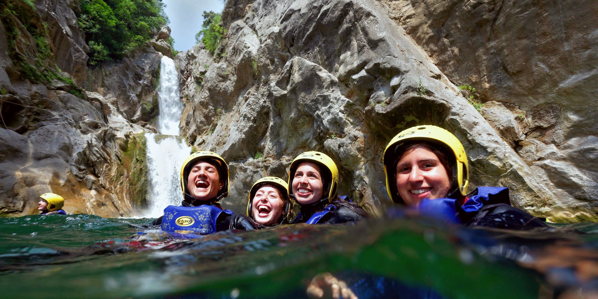 4 amis tout sourire dans l'eau au pied d'une cascade lors d'une activité de canyoning en Ardèche.