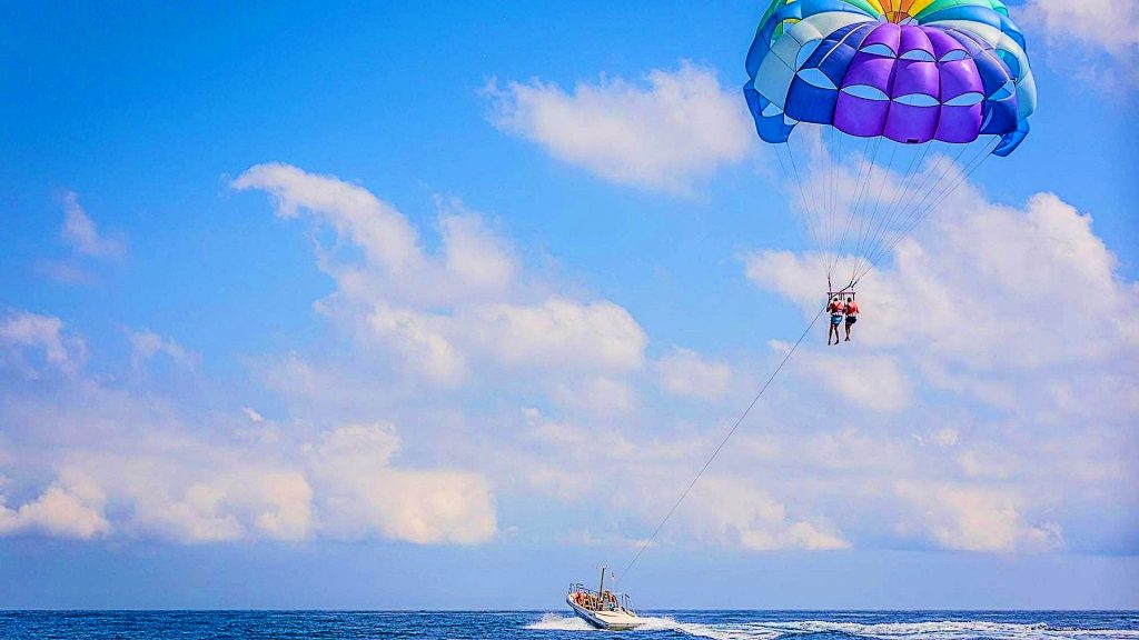 Two people do parasailing near Barcelona with a very colorful parachute, a beautiful outdoor activity near Barcelona. 