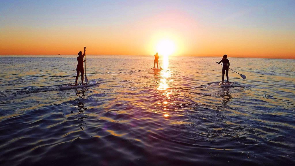 Three persons do SUP in Barcelona during sunset, a beautiful outdoor activity in Barcelona.