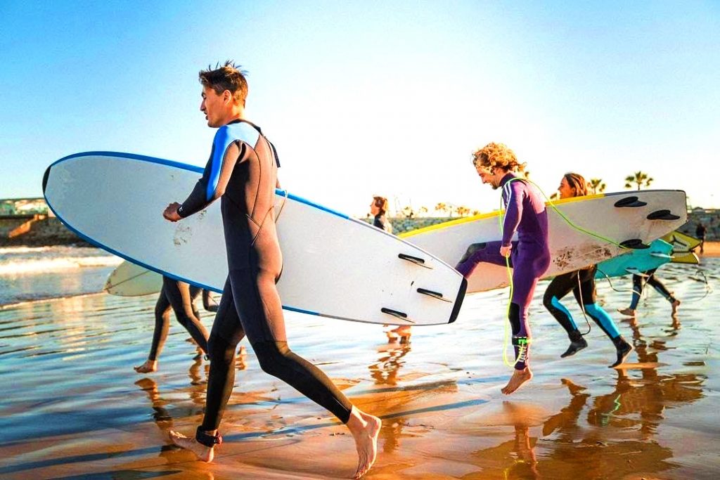 Five guys run with their surfboards under their arms while participating in a surfing lesson in Barcelona, a beautiful outdoor activity in Barcelona.