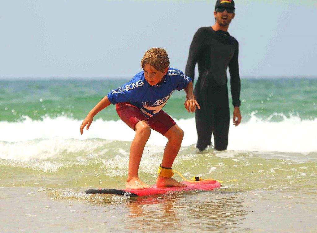 A child stays balanced on the surfboard while the surf instructor gives him advice during the surfing lesson in Hossegor. 