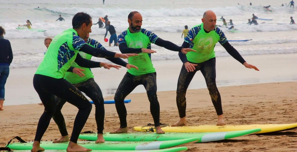 The surf teacher shows how to be on the board to 3 beginners who are taking a surfing lesson.