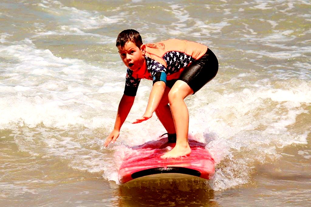 Un enfant heureux sourit pendant qu’il fait du surf à Hendaye.