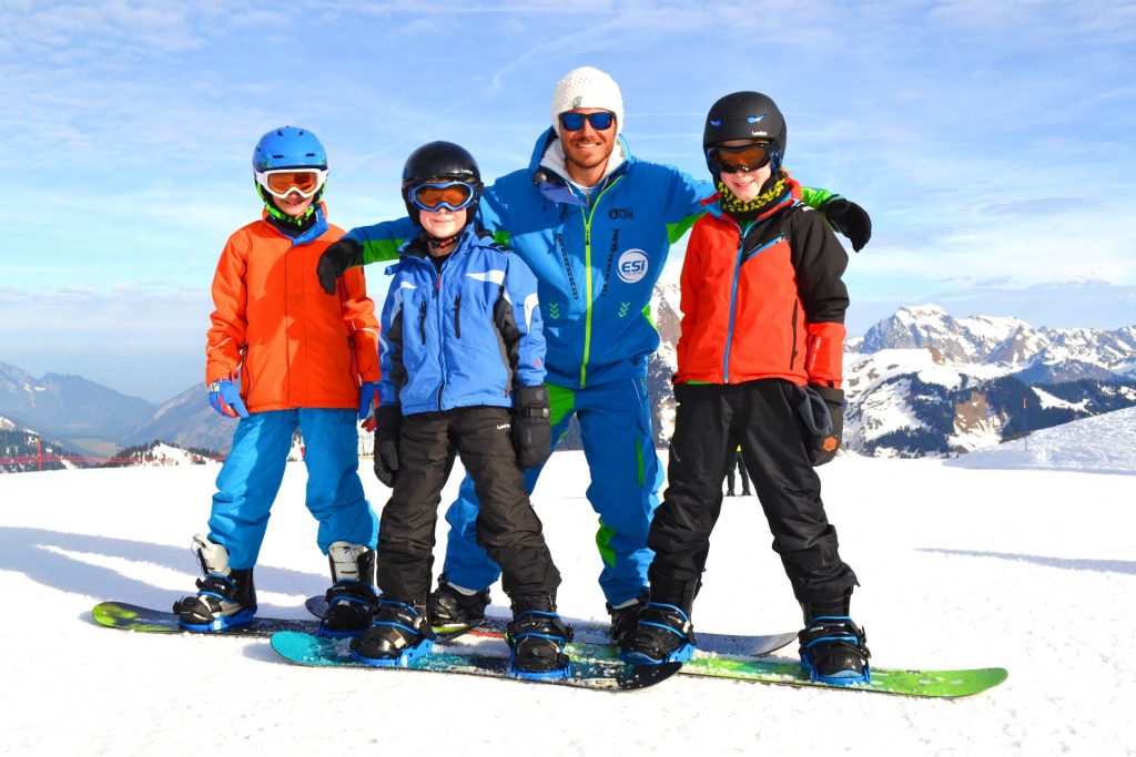 Les enfants sourient avec le moniteur de snowboard.