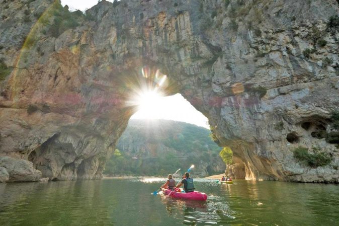 Two people are passing under the Pont d'Arc during a canoe tour on the Ardeche.
