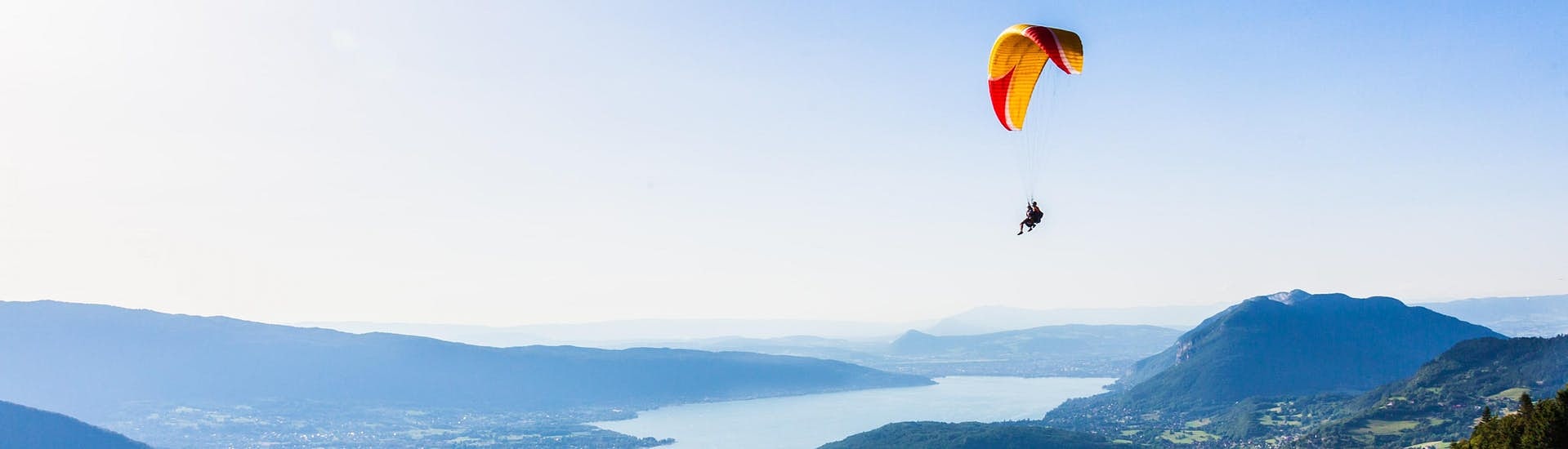 Ein Tandem-Paragleiter fliegt über den türkisblauen See von Annecy.